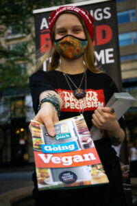 Student wearing a Students Opposing Speciesism t-shirt holding out a Guide to Going Vegan booklet.